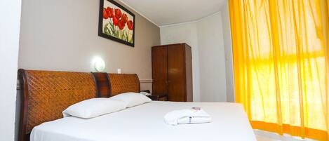 A neatly made bed with white linens, a wooden headboard, and a framed picture of red flowers on the wall.