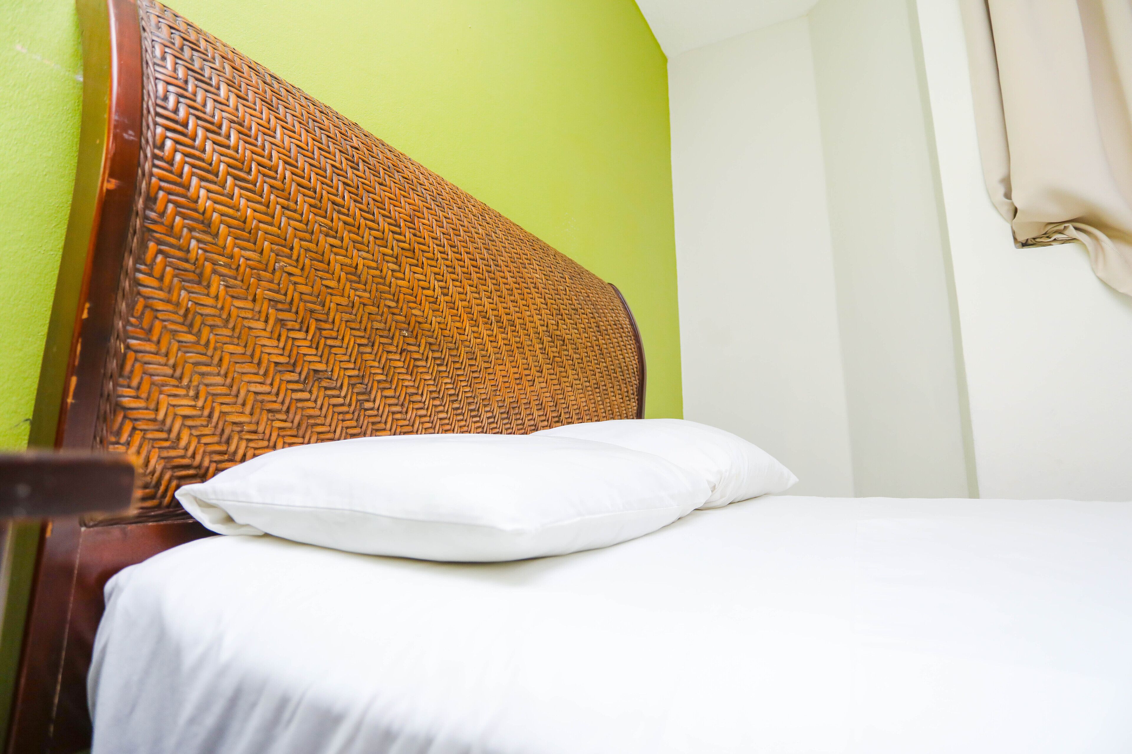 Ein Bett mit einem gewobenen Kopfteil, einem weißen Kopfkissen und einer grünen Wand.