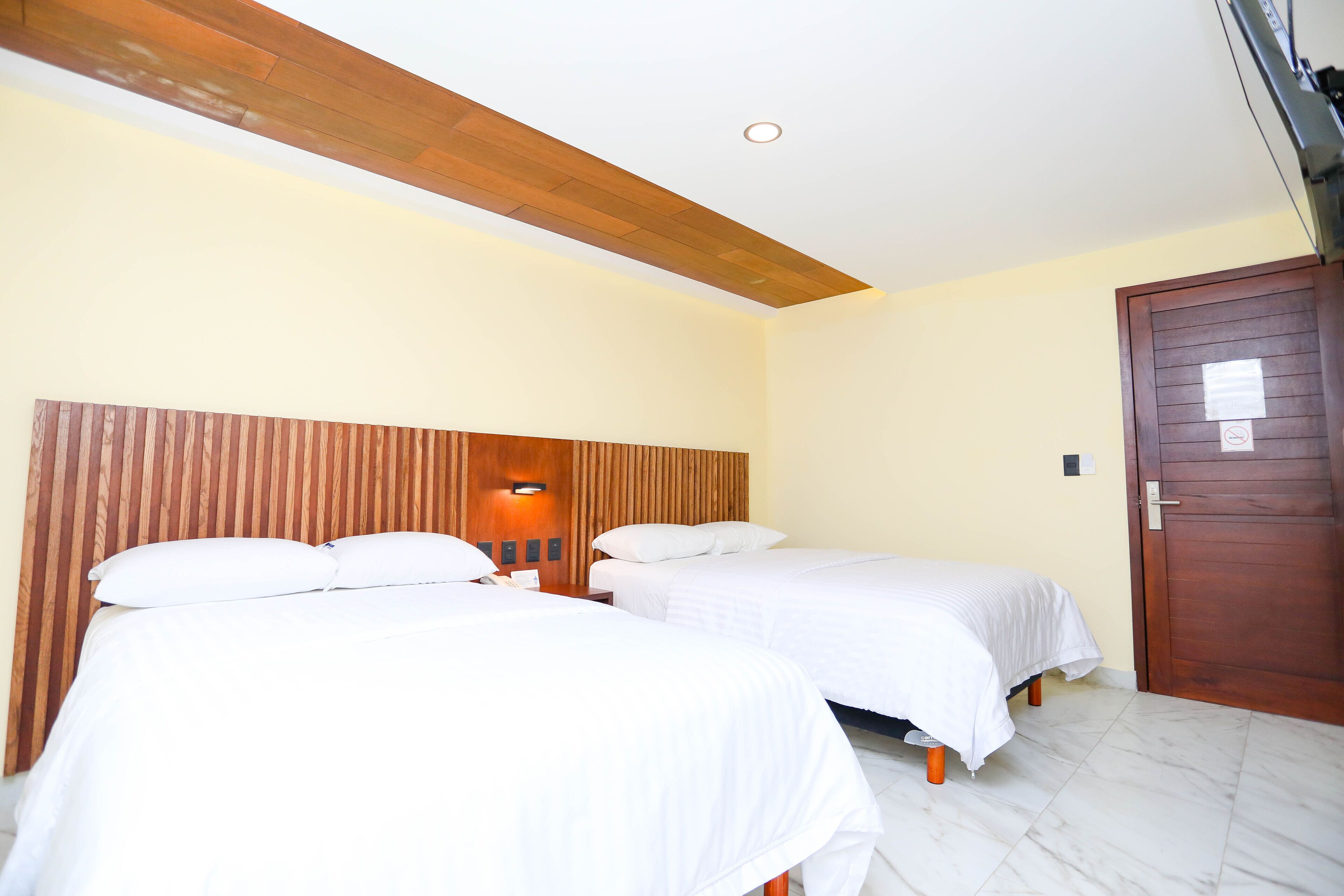 A hotel room with two beds, wooden headboard, white bedding, and a wooden door.