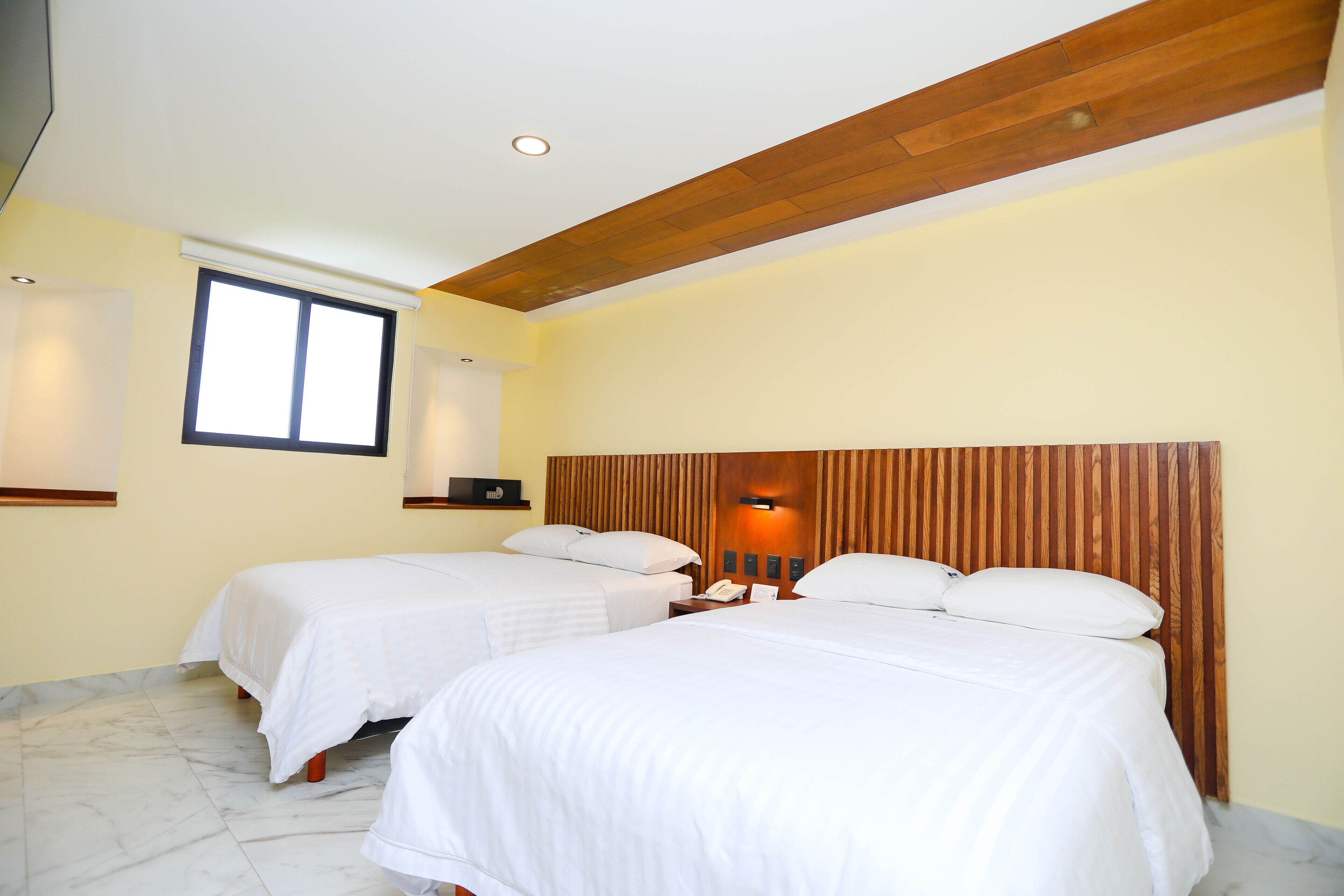 Ein Hotelzimmer mit zwei Betten, einem Holzkopfstück, einem kleinen Schreibtisch und einem Fenster.