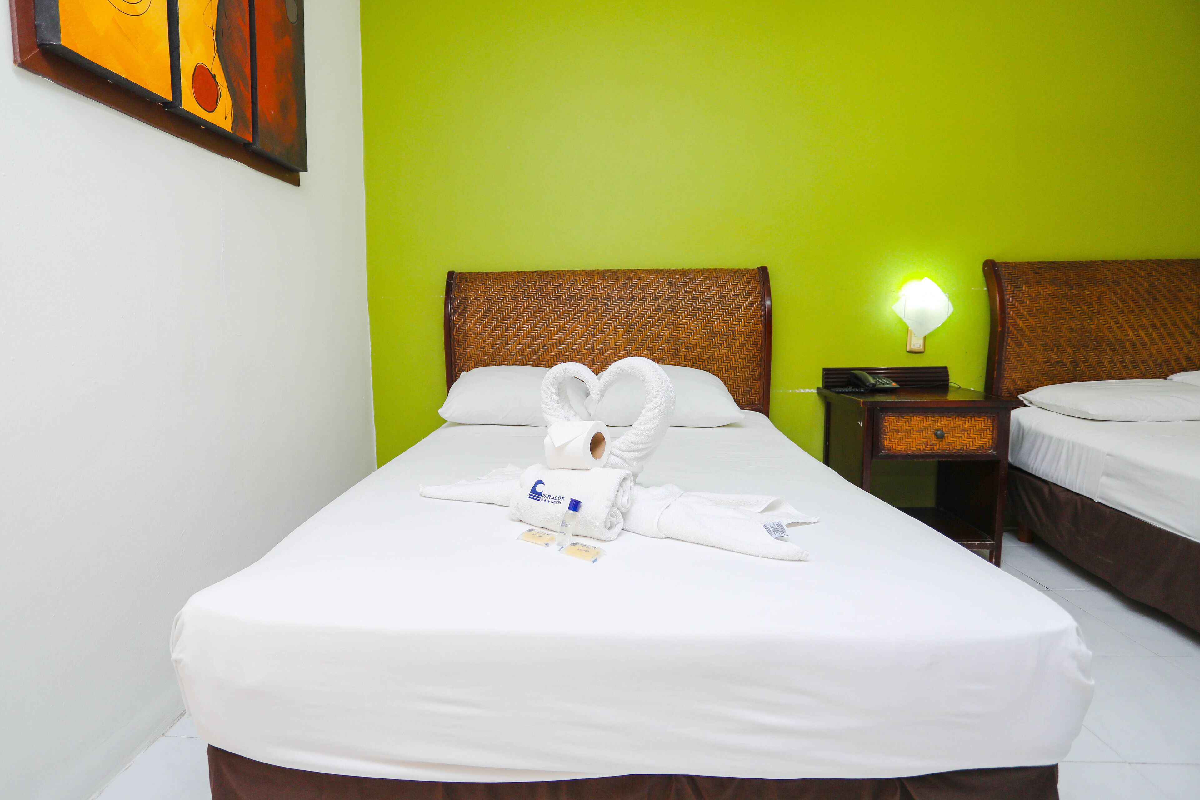 Una habitación de hotel con una cama, una mesita de noche con lámpara y un cuadro en la pared.