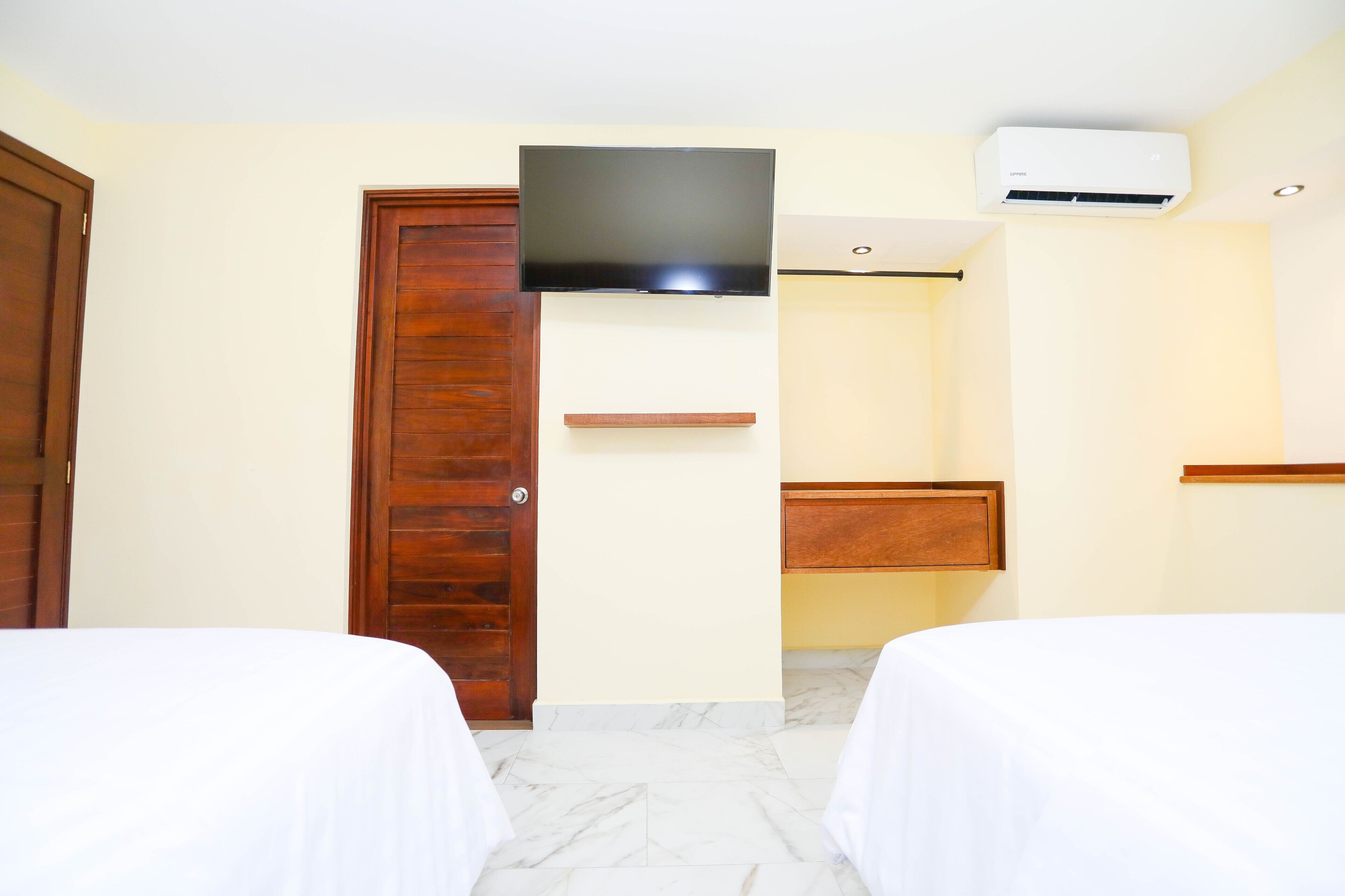 A hotel room with two beds, a television mounted on the wall, a wooden door, and a small shelf.