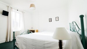 Hotelkamer met een bed, nachtkastje, lamp, radiator, televisie en een raam met gordijnen.
