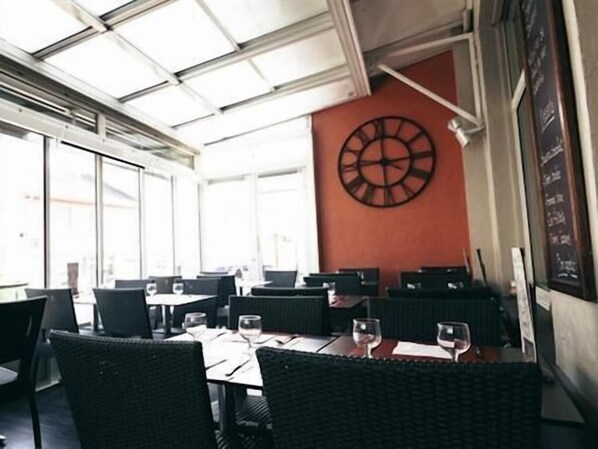Un área de comedor interior con mesas y sillas, un reloj de pared grande y una pizarra de menú.