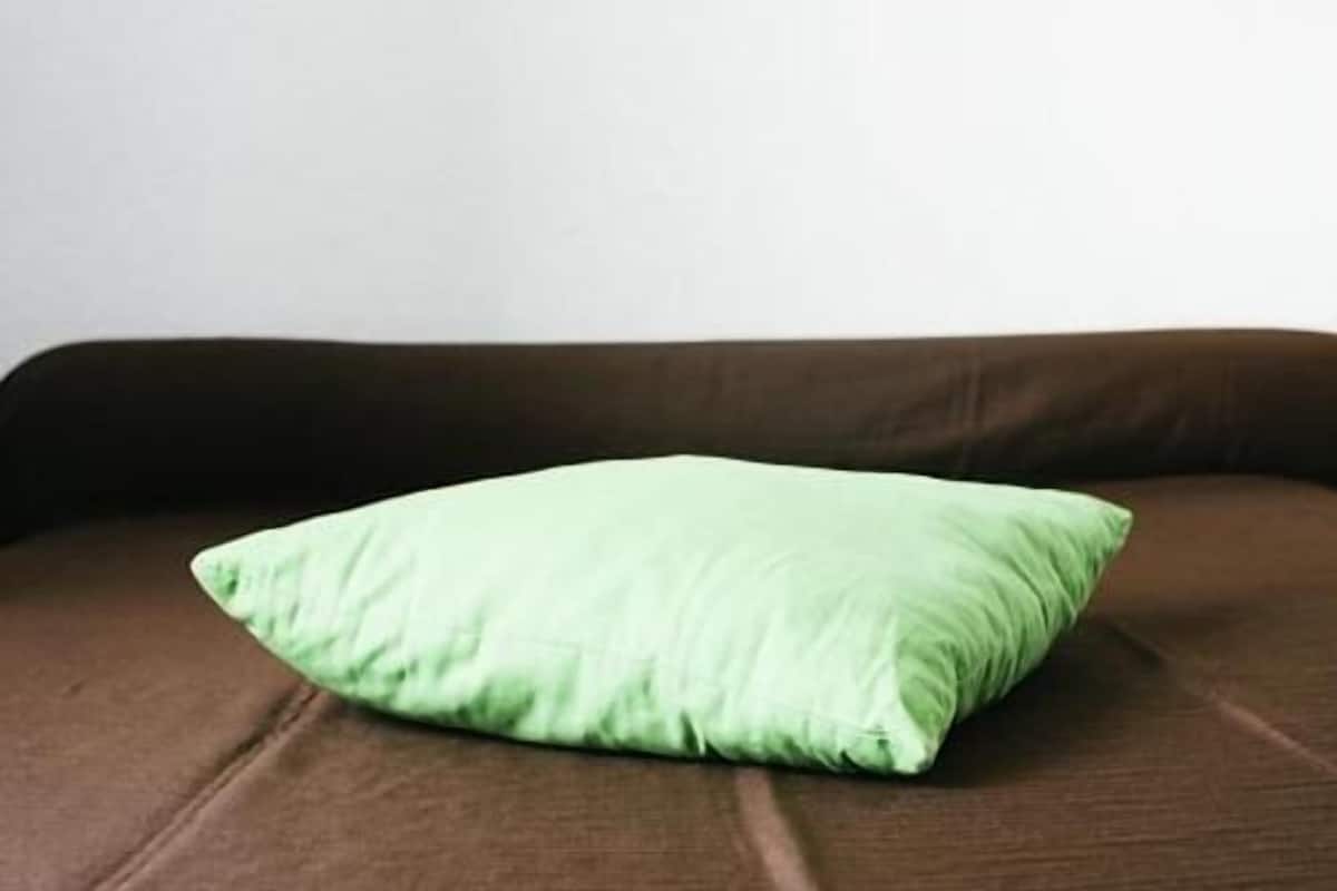 Un cojín verde sobre un sofá marrón frente a una pared lisa.