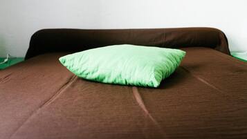 Ein Bett mit brauner Bettdecke und grünem Kopfkissen, zwei gerahmte Bilder an der Wand und ein grüner Nachttisch.