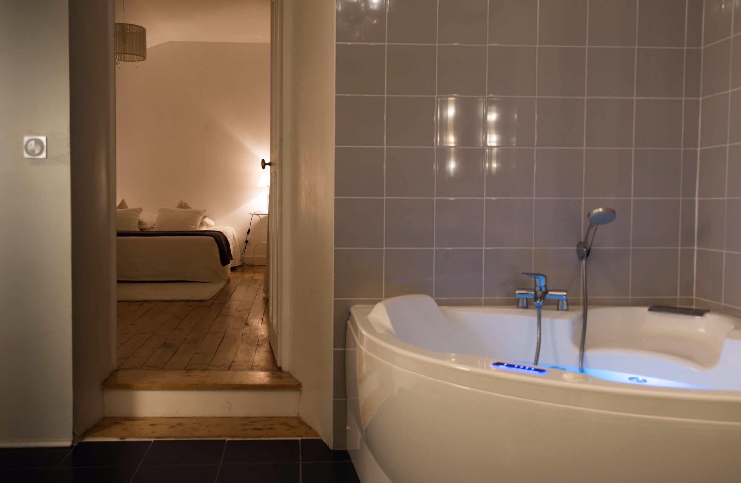 A modern bathroom with a large bathtub, tiled walls, and a wooden floor.