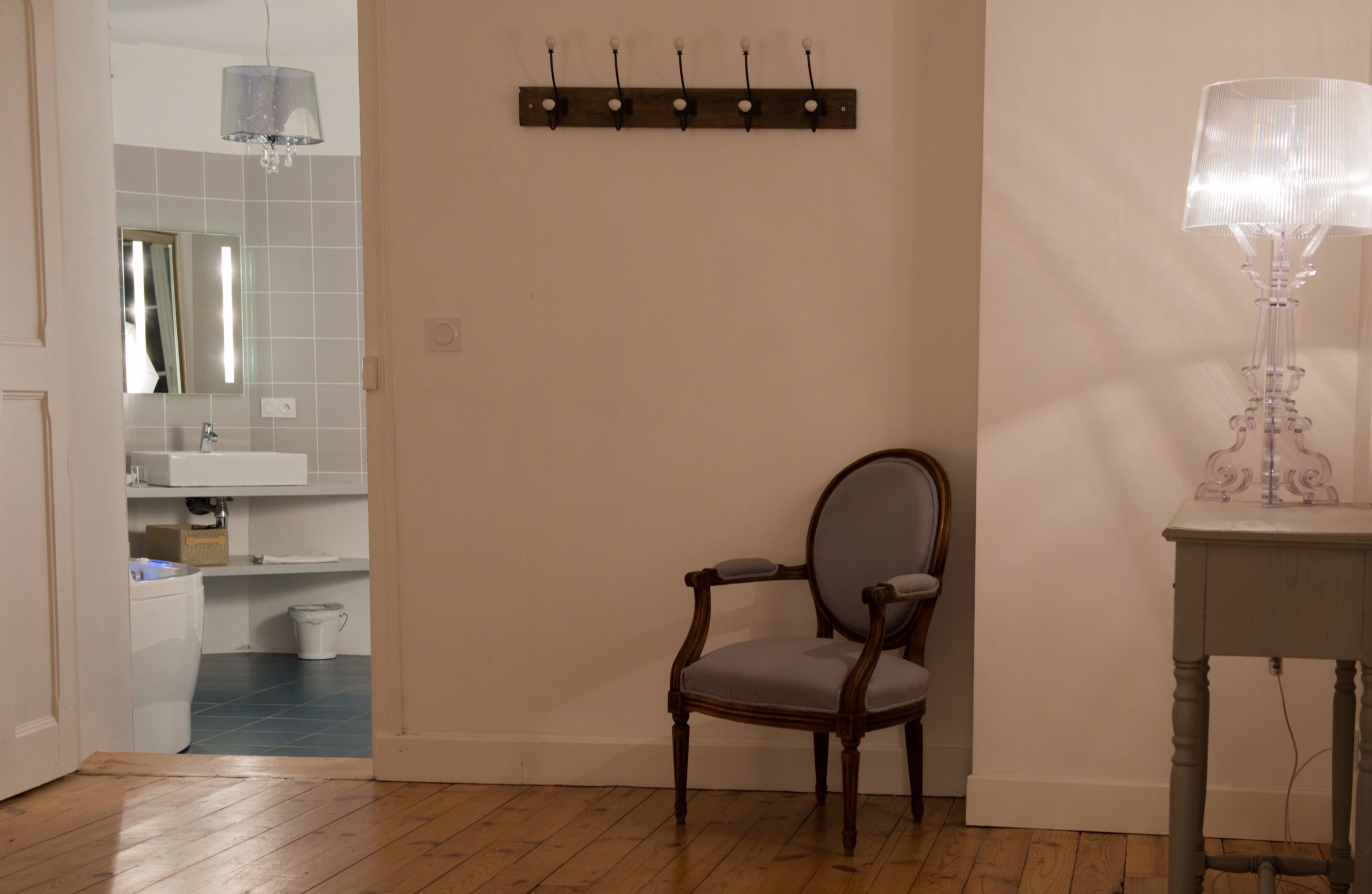 Un baño con suelo de madera, una silla, una mesa con lámpara y un perchero para toallas.