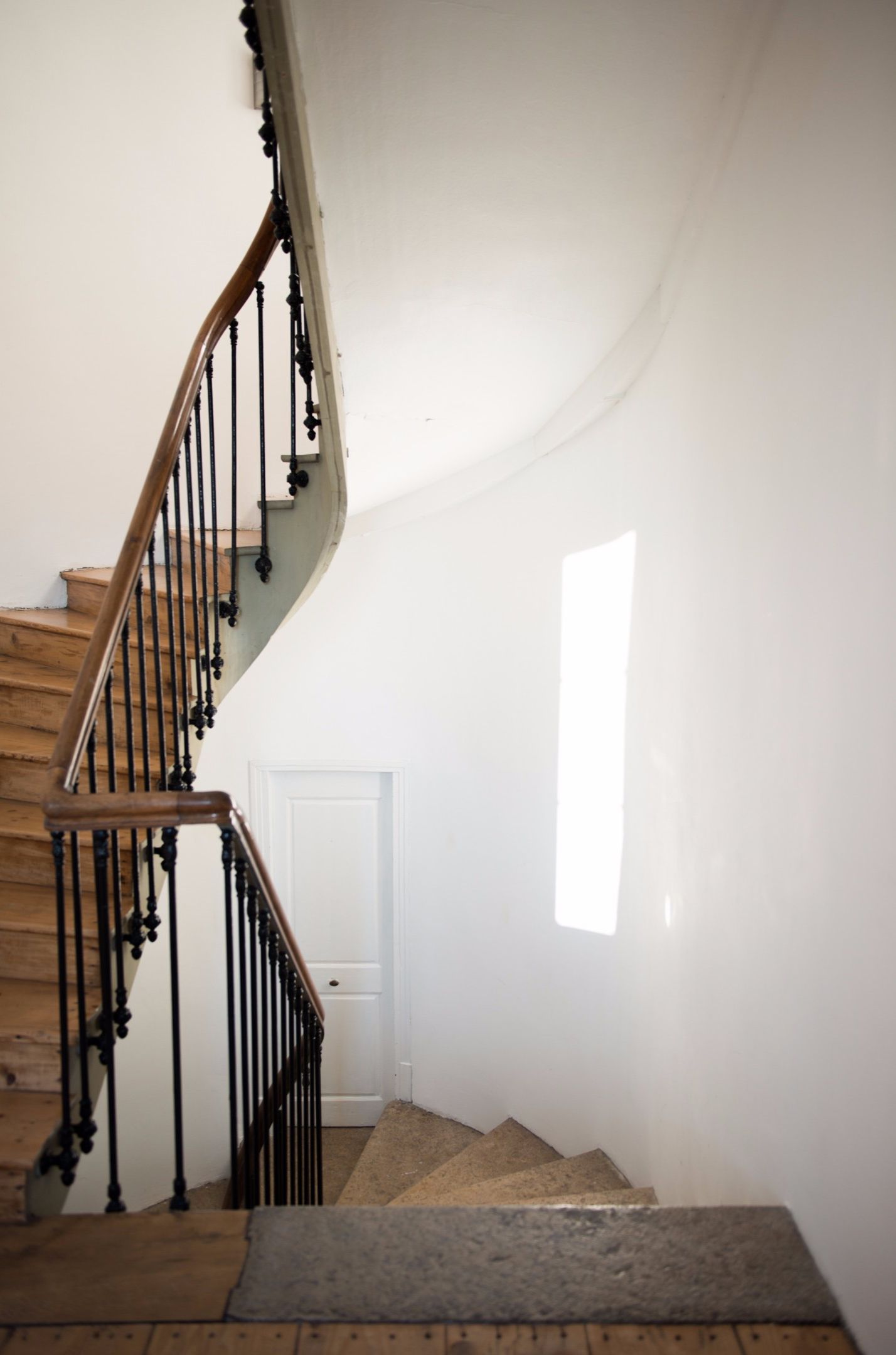 Una escalera de madera con barandillas negras que lleva a una puerta blanca.