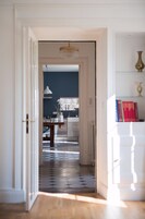 Un pasillo que conduce a una cocina con candelabro, un comedor y una estantería con libros y objetos decorativos.