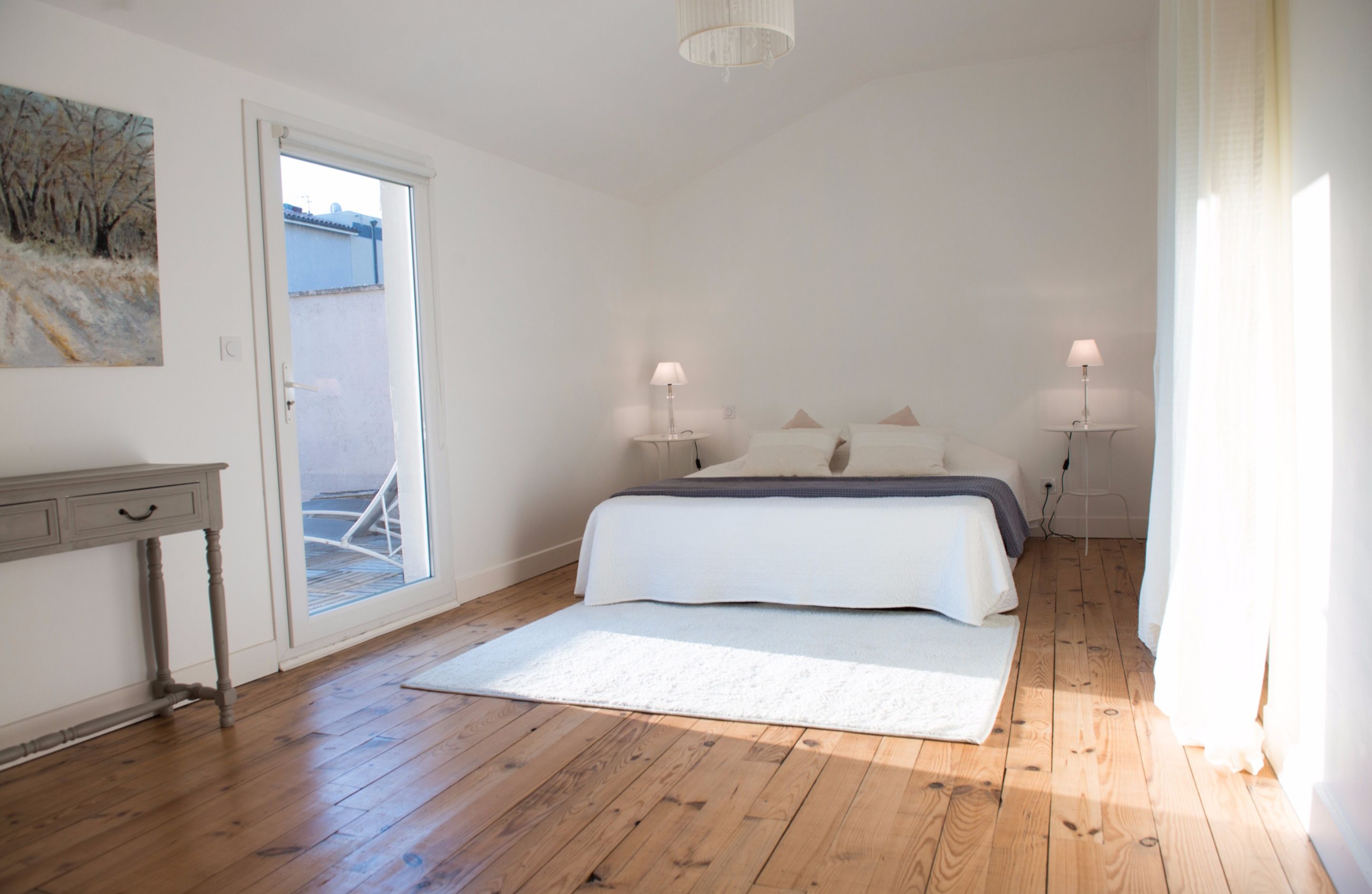 A bedroom with a bed, bedside lamps, a nightstand, a door leading outside, and a painting on the wall.