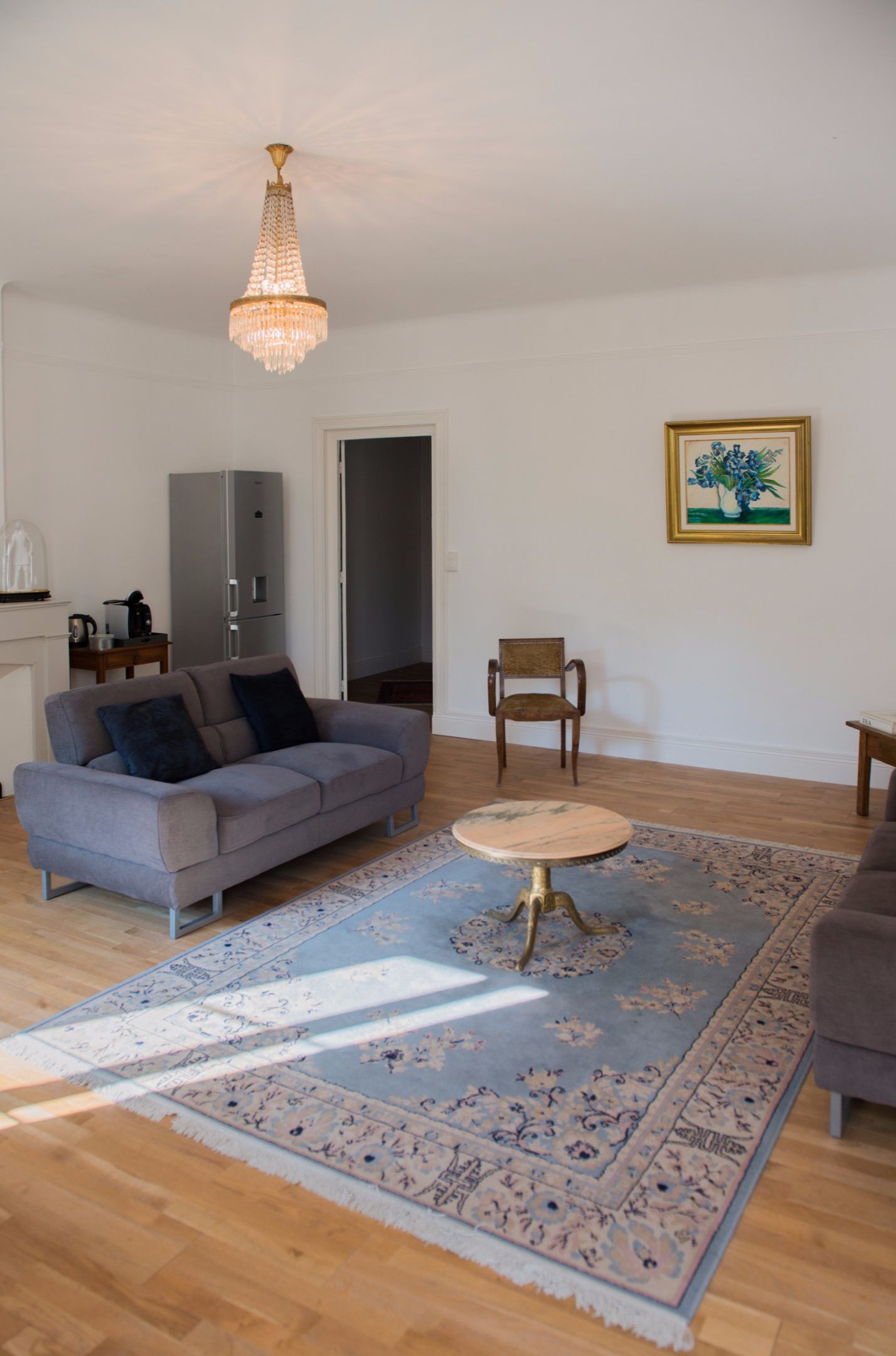 A living room with a grey sofa, a round coffee table, a chandelier, a framed picture, and a wooden cabinet.