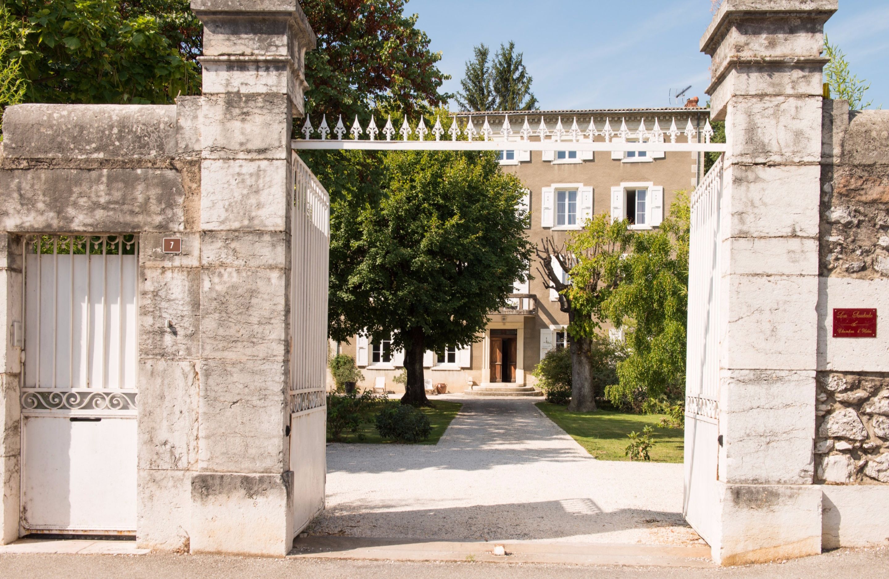 Un portail en pierre mène à un bâtiment à la façade traditionnelle, avec un chemin dégagé et un jardin bien entretenu.