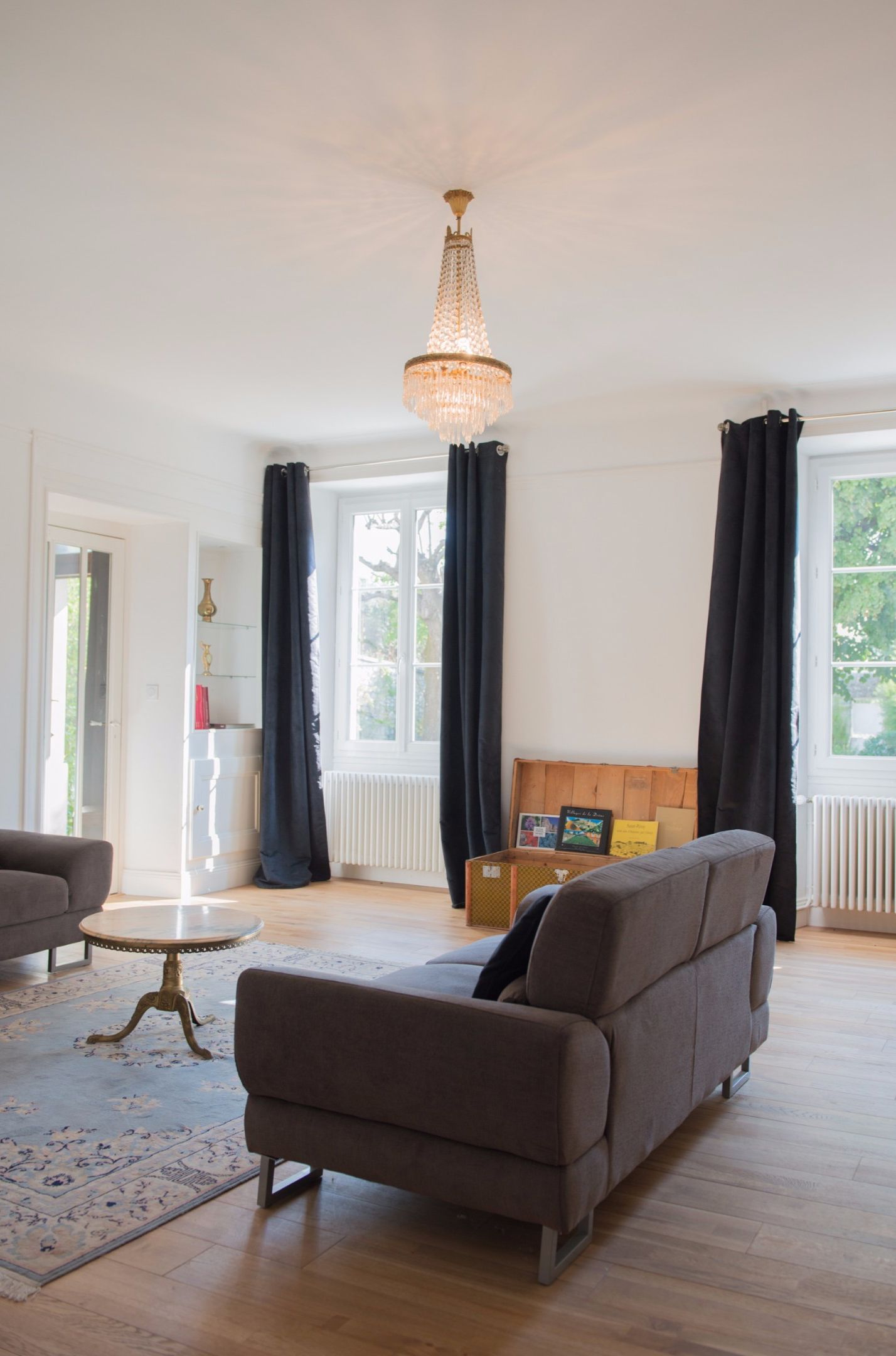 A living room with a chandelier, a sofa, a small round table, and a window with curtains.