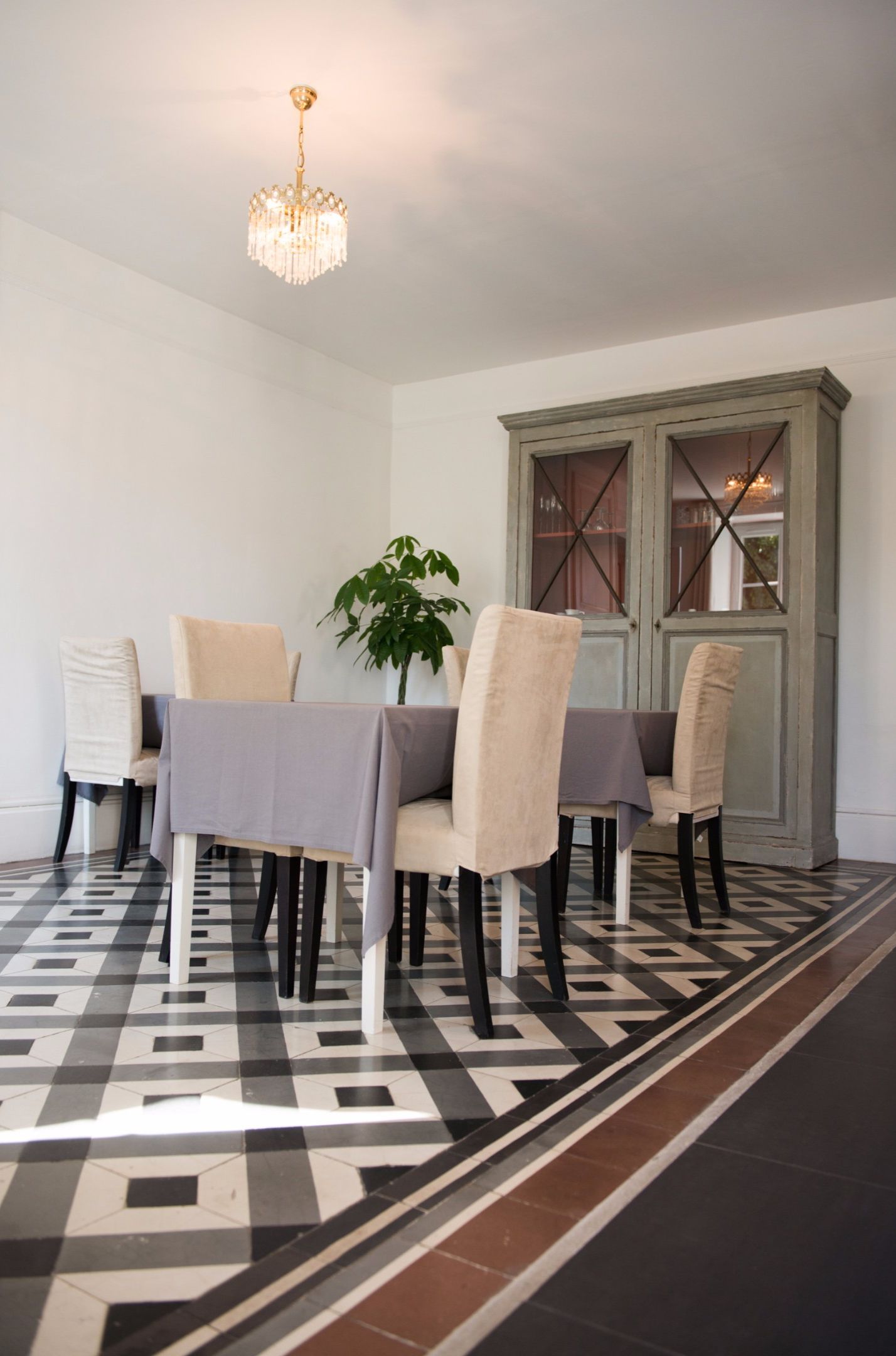 A dining area with a table set for four, surrounded by upholstered chairs, a chandelier, and a patterned floor.