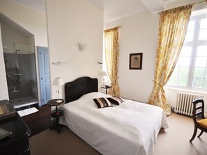 A hotel room with a bed, a desk, a chair, a lamp, a picture on the wall, and a window with curtains.