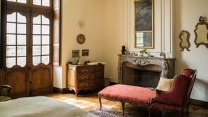 Ein Zimmer mit Holztür, Kamin, einem roten, gepolsterten Sessel und einem Bett.