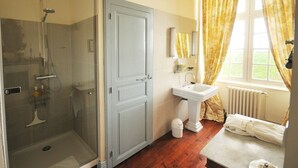 Ein Badezimmer mit Duschkabine, freistehendem Waschbecken, Spiegel und einem fenster mit Vorhängen.