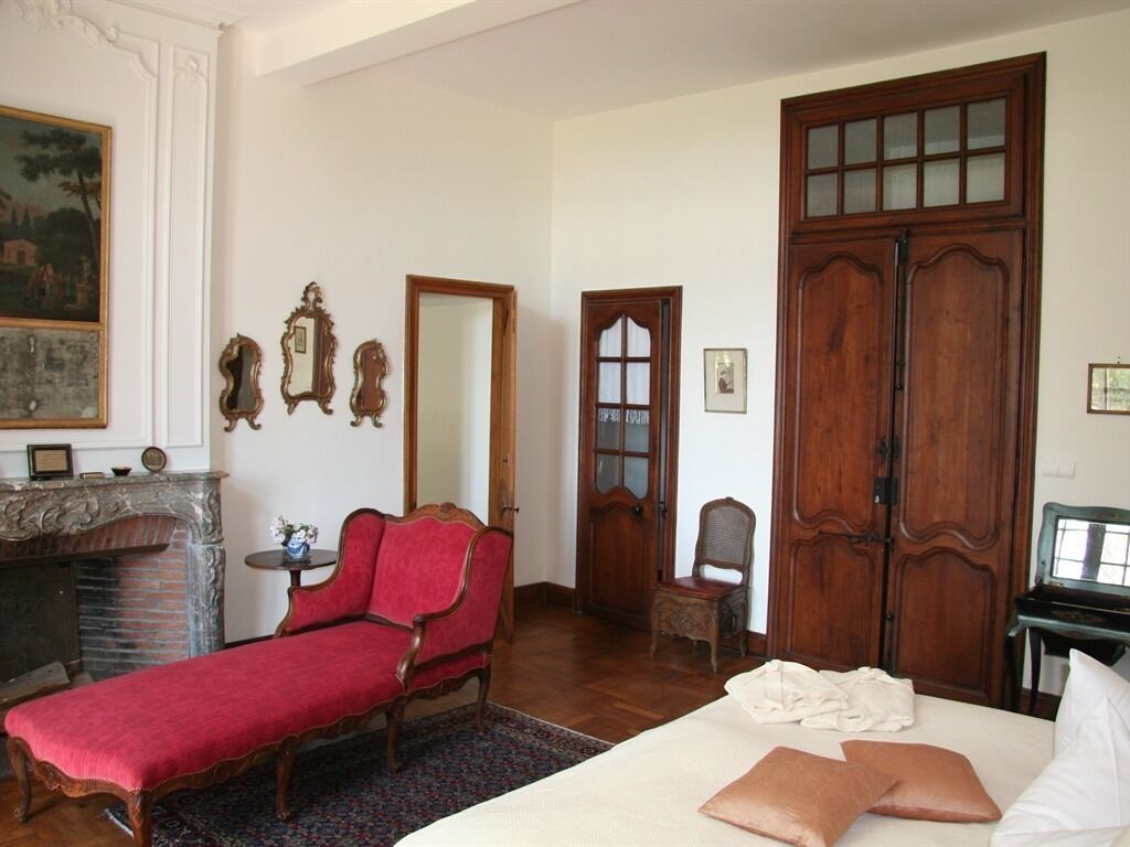 A room with a red sofa, a bed with pillows, a fireplace, and wooden doors.
