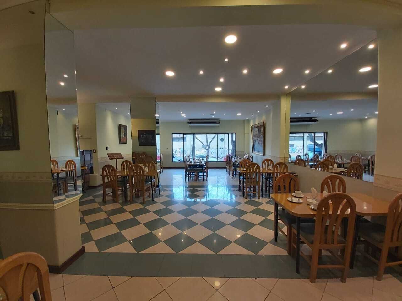 A spacious dining area with checkered flooring, multiple tables and chairs, and large windows allowing natural light.
