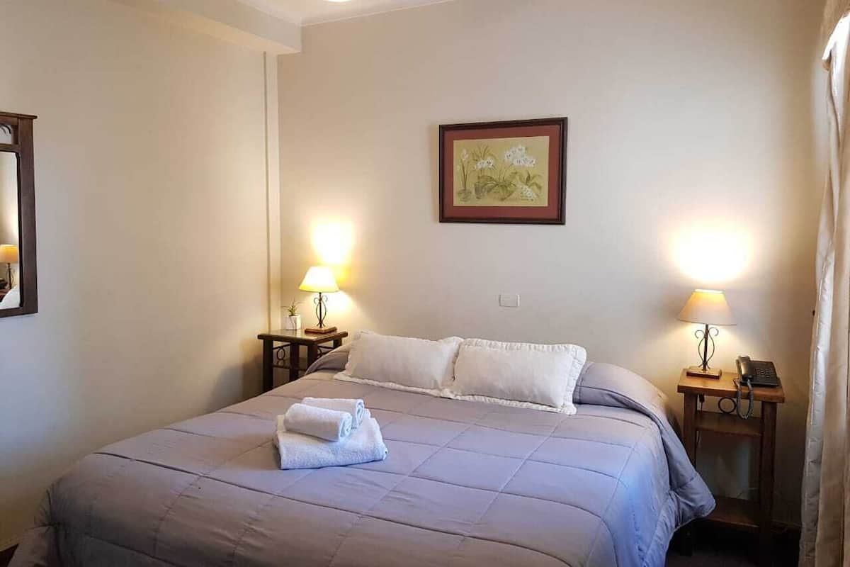 A neatly made bed with a folded towel, two bedside lamps, and a framed picture on the wall.