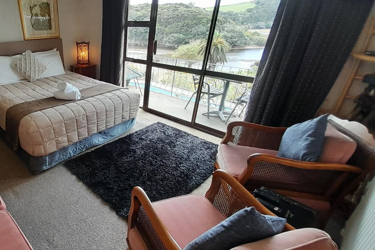 A bedroom with a bed, bedside lamps, a view of the outdoors, a desk, and a chair.