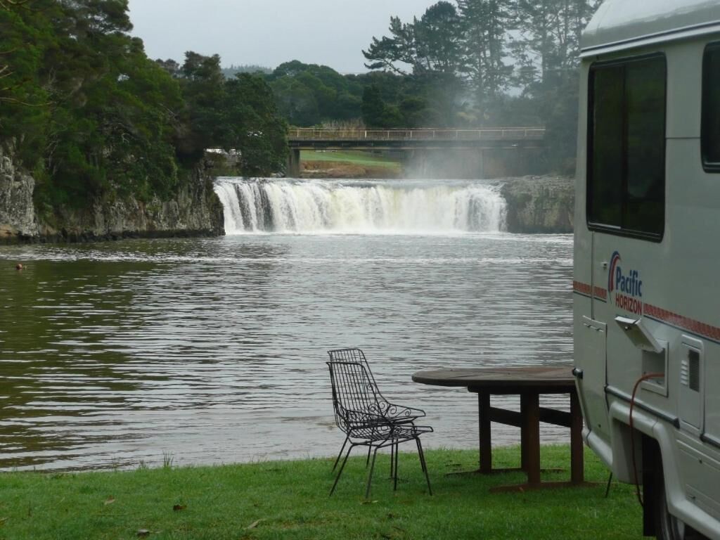 A waterfall, a picnic table, and a chair by a river.