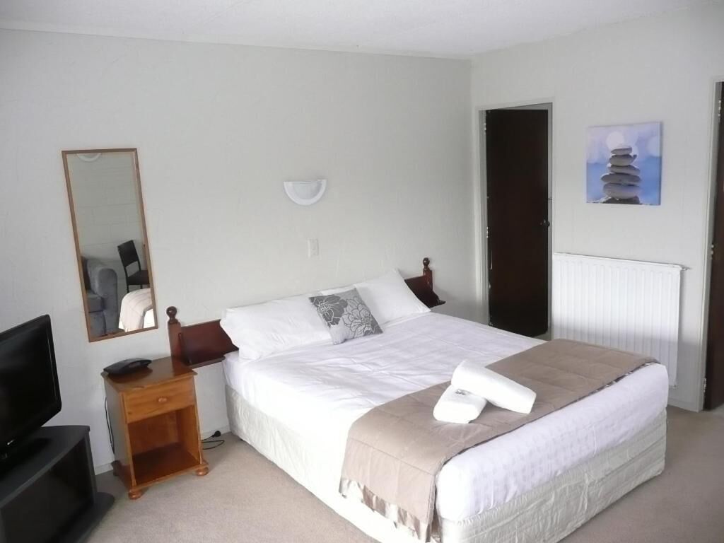 Habitación de hotel ordenada con cama, televisor, mesita de noche y espejo.