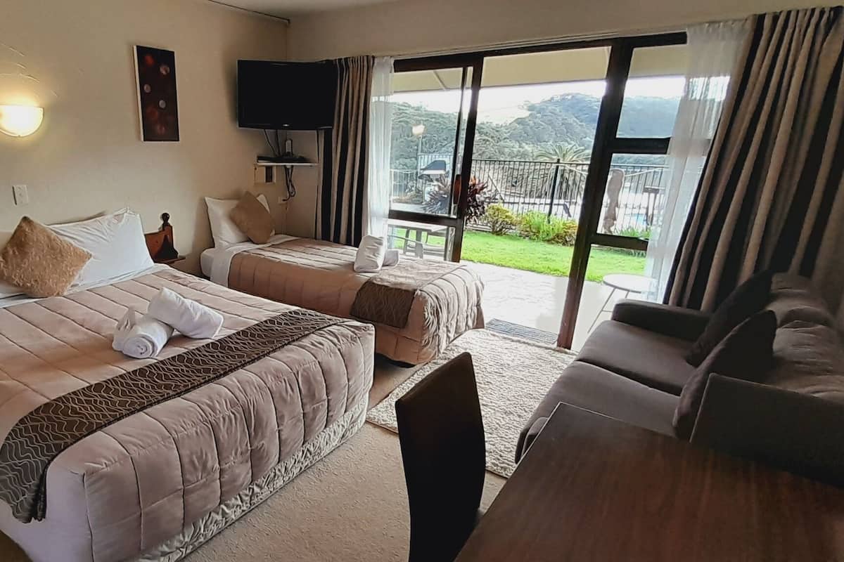 A hotel room with two beds, a TV, a balcony with a view, and a seating area.