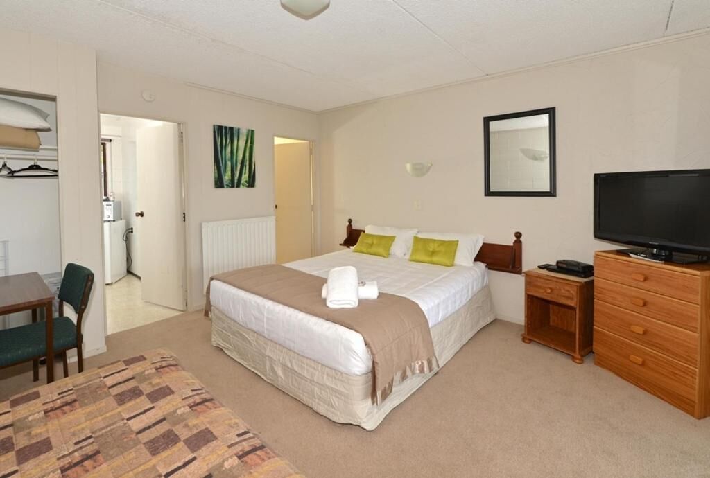 A hotel room with a bed, a television, a dresser, a desk, and a chair.