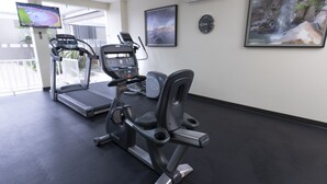 Un gimnasio con cintas de correr y una máquina elíptica, un televisor en la pared y un reloj.