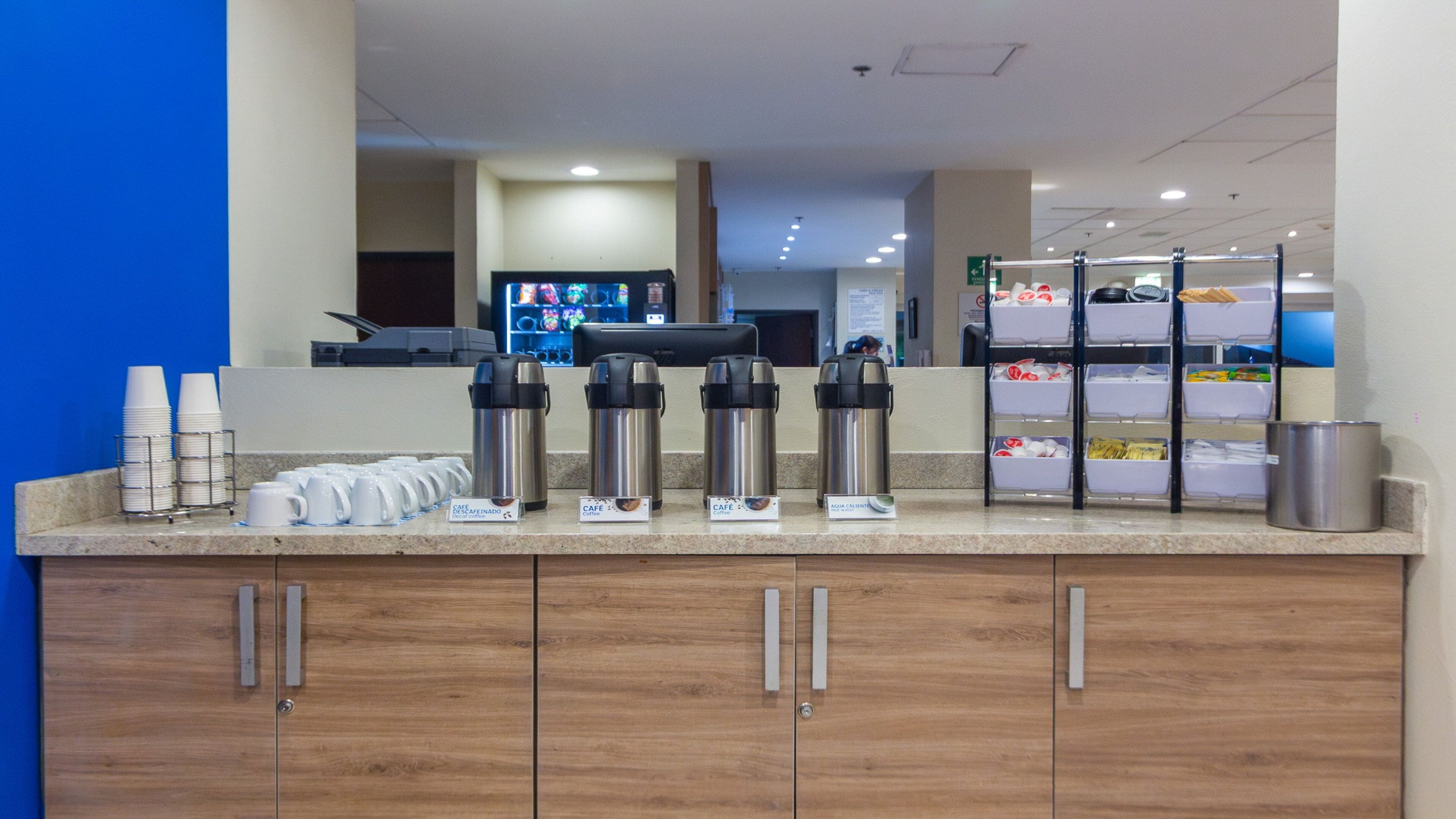 A hotel breakfast area with coffee makers, cups, and a self-service beverage station.