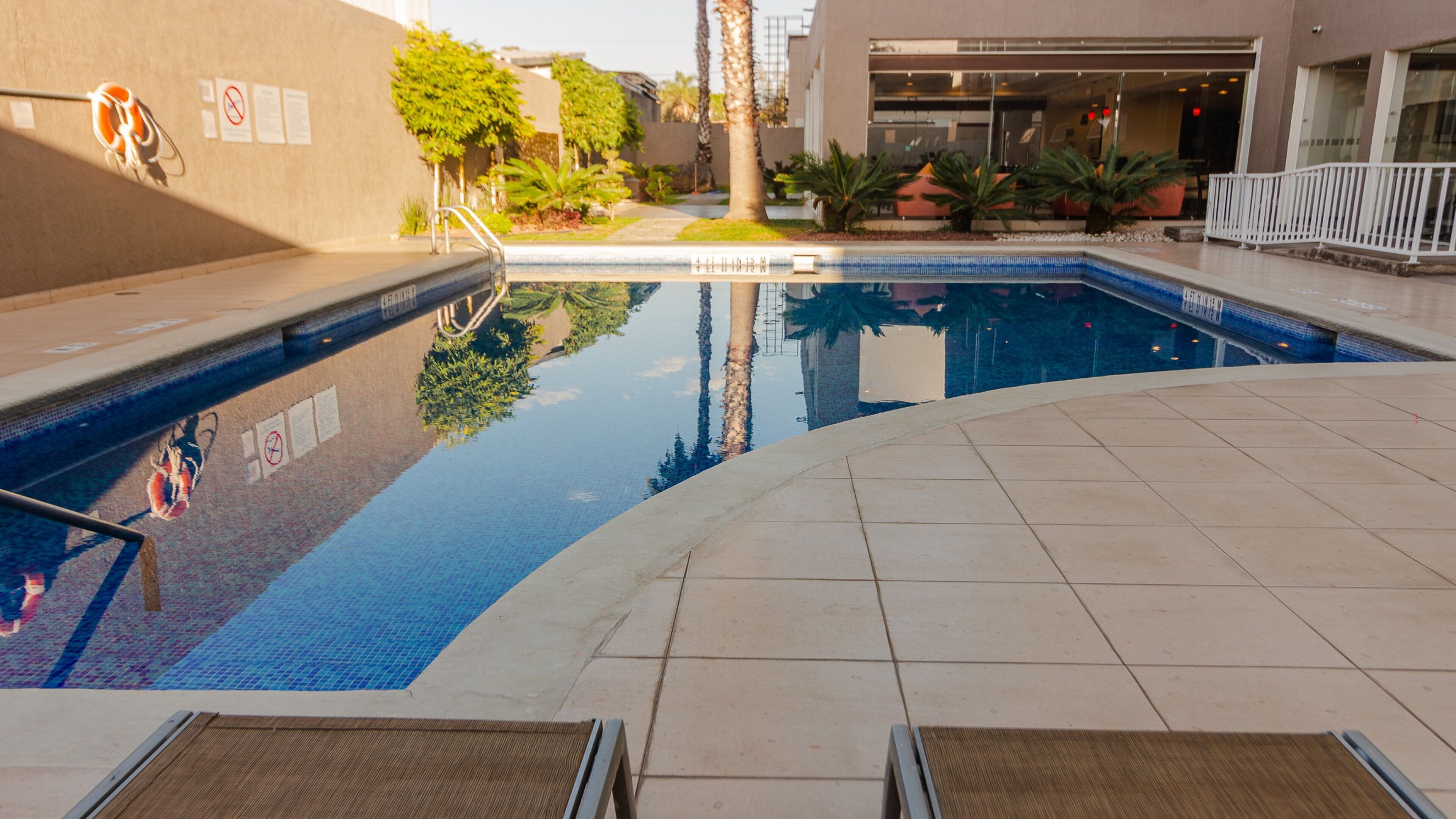Una piscina con borde de baldosas, rodeada por un edificio de fachada de vidrio.