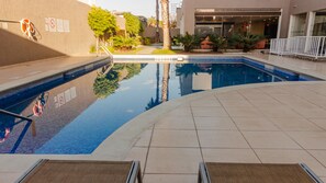 A swimming pool with a tiled deck, surrounded by a building with a glass facade. - Holiday Inn Express Guadalajara Aeropuerto by IHG (El Salto)