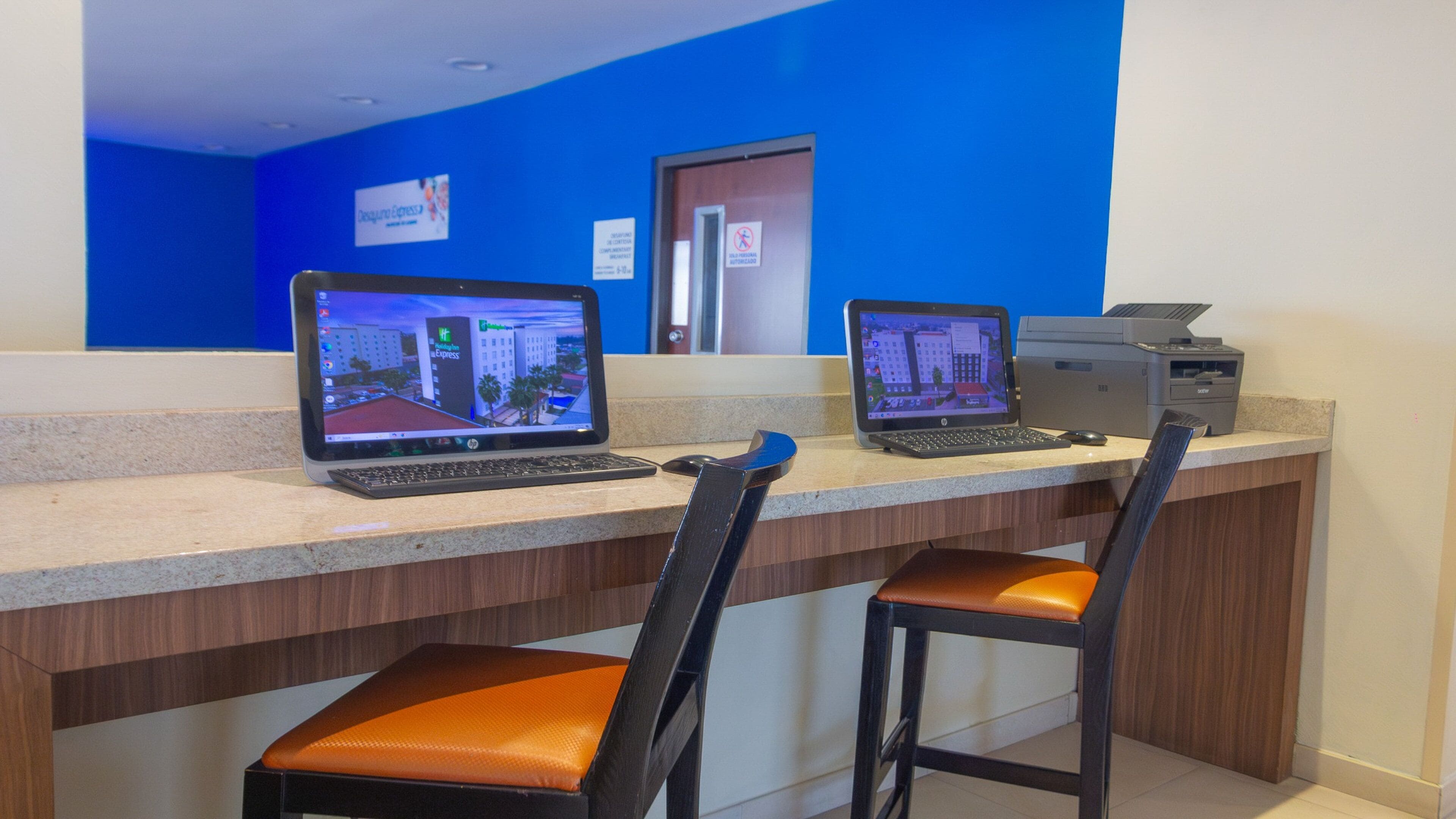 A reception desk with two laptops, a printer, and two chairs.
