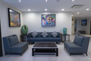 Um hall moderno com um sofá azul, duas poltronas, uma mesa de centro e dois vasos decorativos.