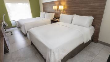 A hotel room with two beds, a desk with a chair, and a window with blinds.