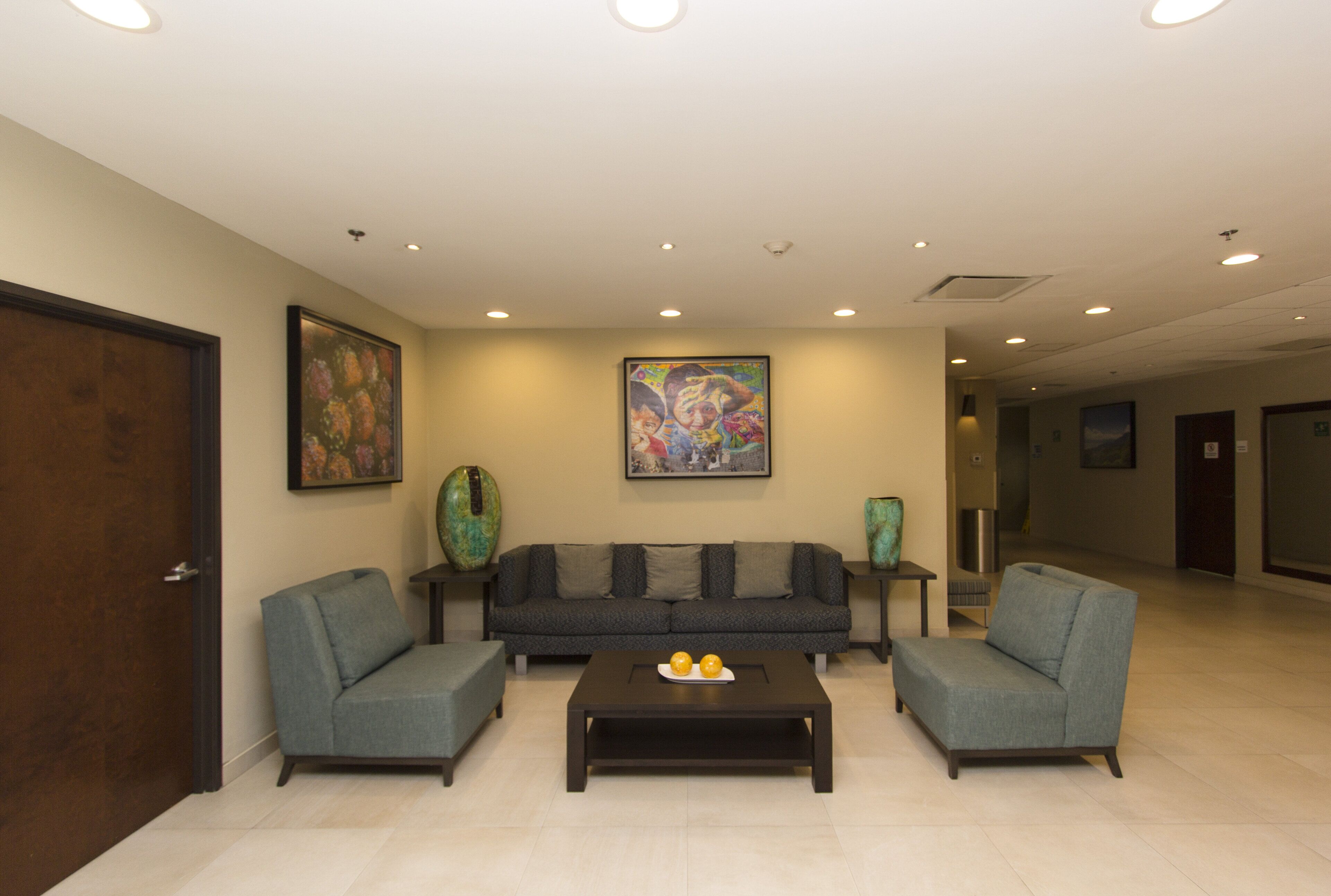 A lobby with a sofa set, two armchairs, a coffee table, and artwork on the walls.