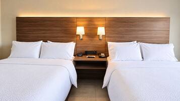 Quarto de hotel com duas camas, cabeceira de madeira, abajures, mesa de cabeceira com telefone e controle remoto, e um relógio.