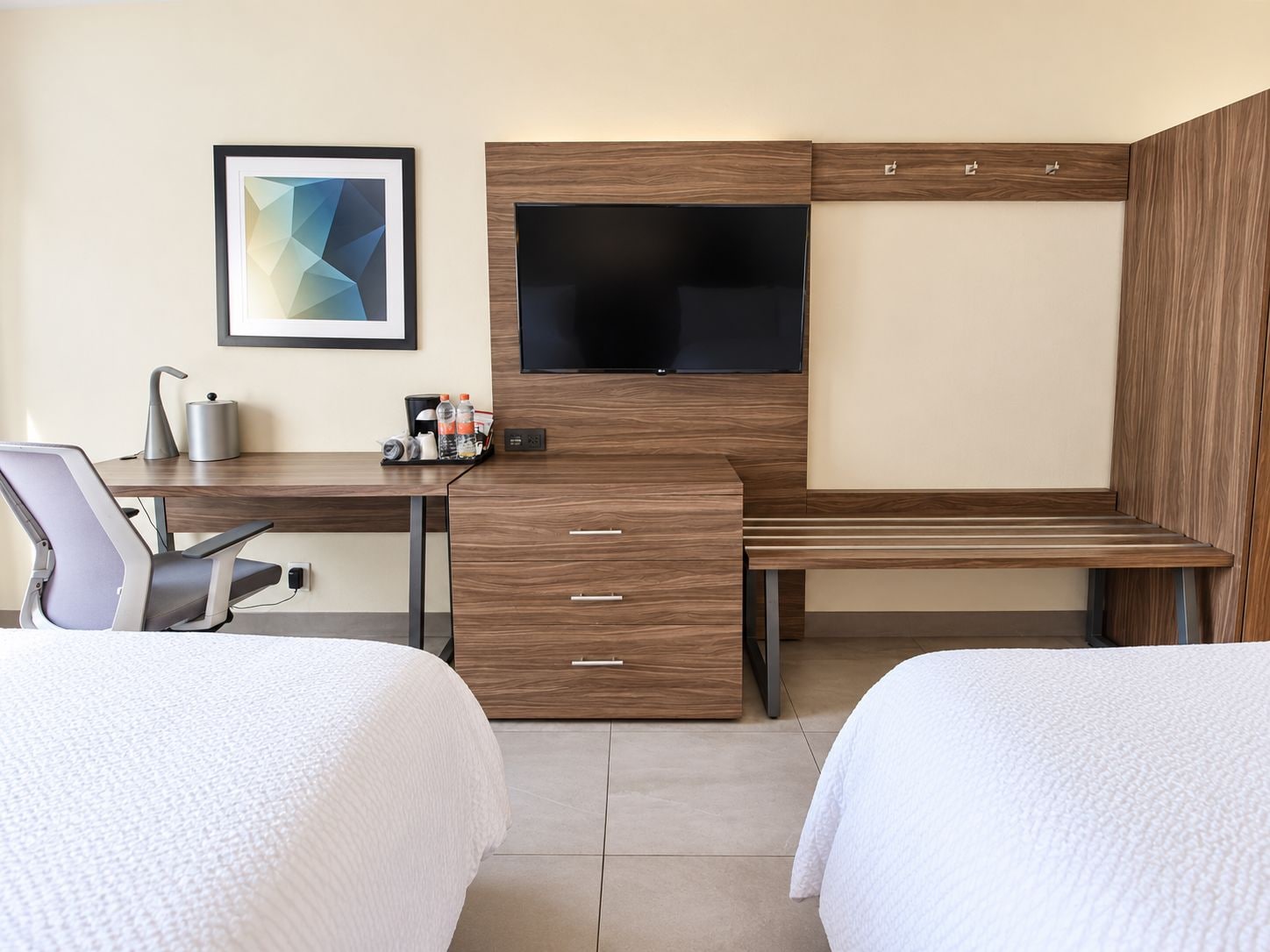 Ett hotellrum med en säng, ett skrivbord, en stol, en tv och en inramad tavla på väggen.