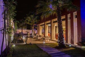 A well-lit outdoor patio area with seating, palm trees, and a stone pathway.