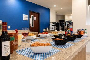 A buffet setup with various food items and beverages, including a bottle of wine, on a counter with checkered placemats. - Holiday Inn Express Guadalajara Aeropuerto by IHG (El Salto)