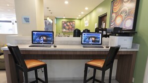 Una zona de recepción con dos taburetes, un mostrador con dos computadoras HP, una impresora Samsung y un gran elemento decorativo en la pared.