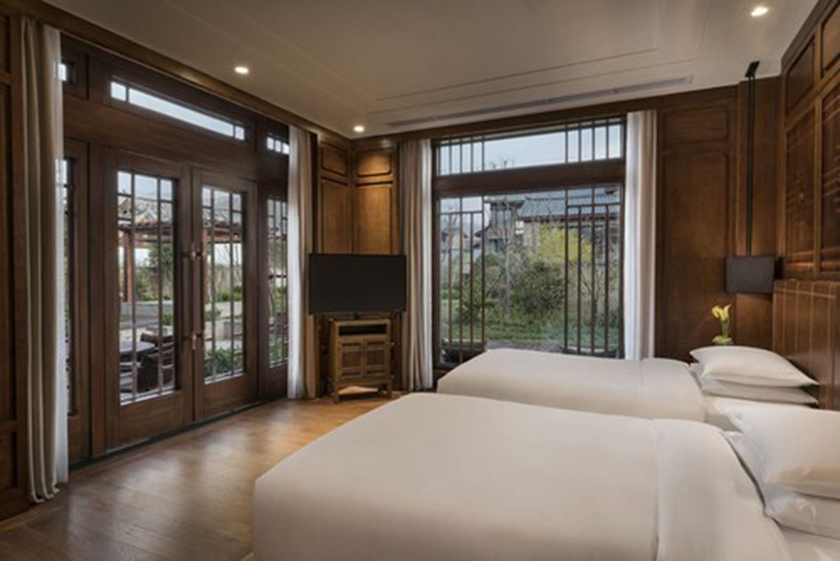 A hotel room with two beds, a television, and large windows offering a view of the outdoors.