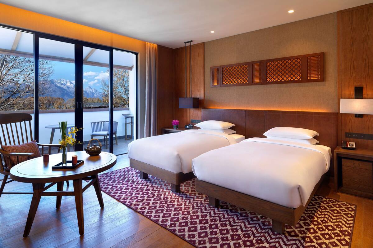 Ein Hotelzimmer mit zwei Betten, einem Esstisch und Blick auf Berge.
