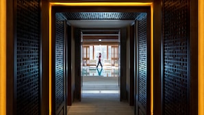 A corridor with traditional wooden lattice doors leading to a bright room with a person walking. - Jinmao Purelax Lijiang -The Unbound Collection by Hyatt (Lijiang)