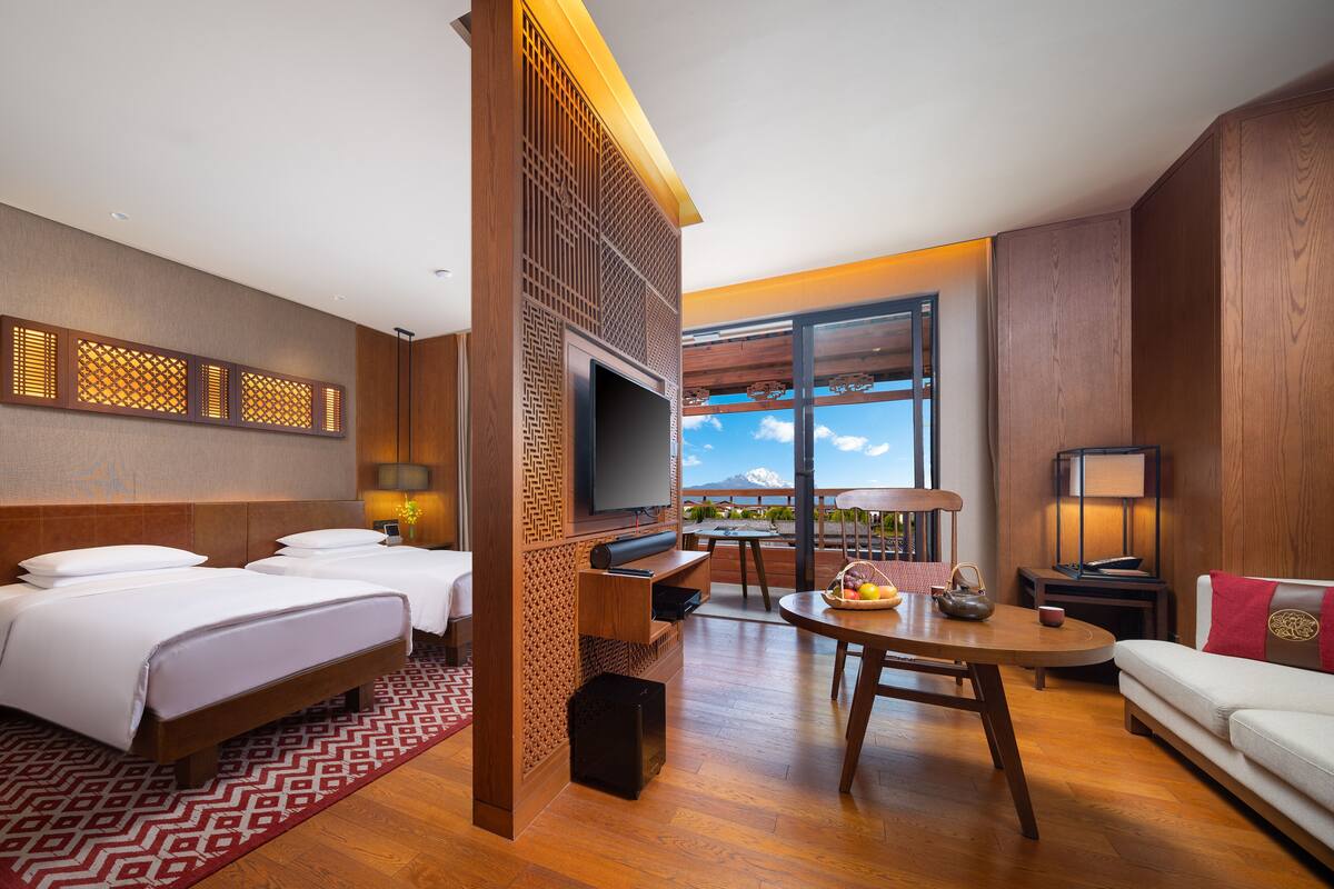 Ein Hotelzimmer mit zwei Betten, einem Fernseher, einem Esstisch und einem Sofa.