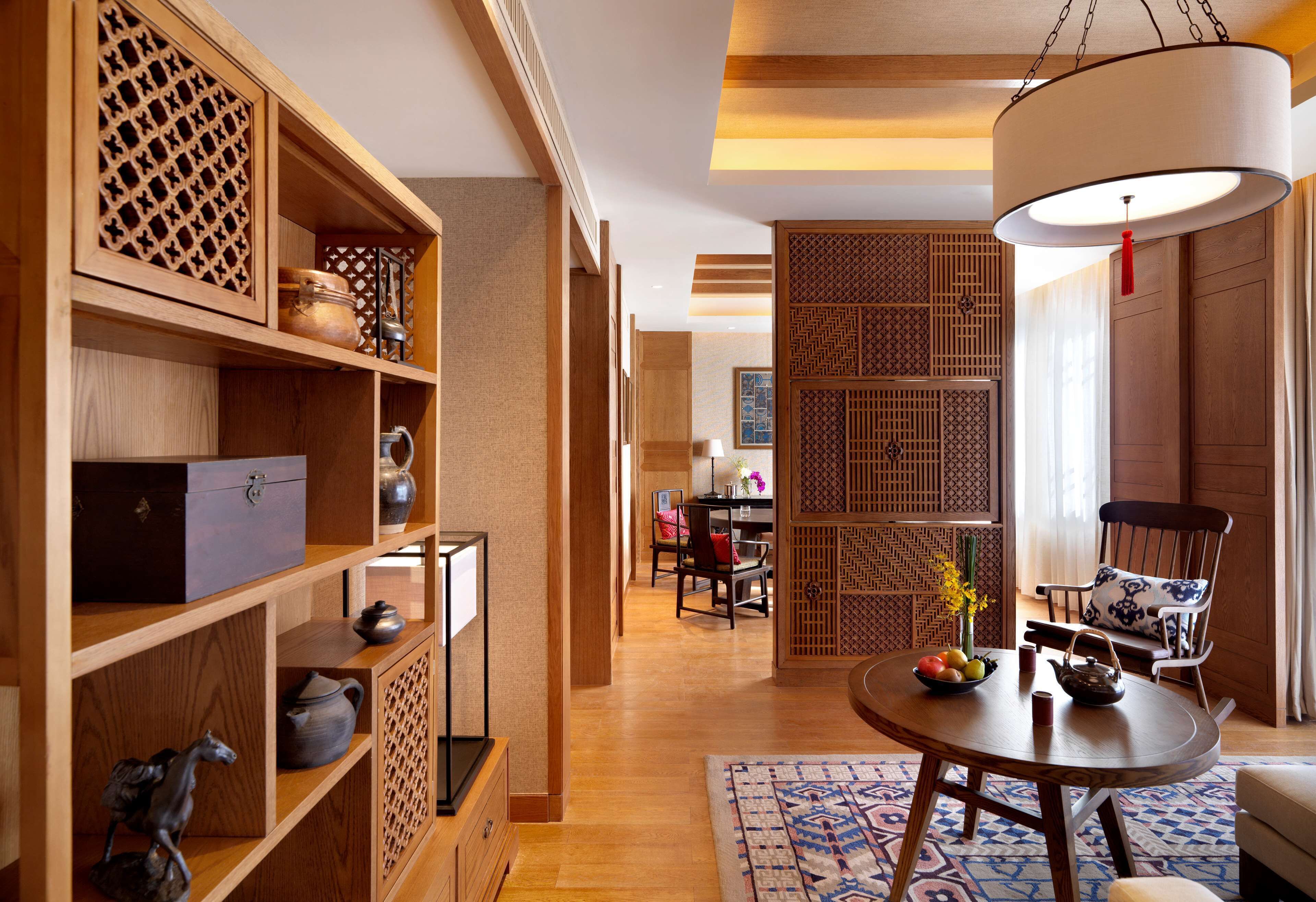 Une pièce de style japonais traditionnel, avec des étagères en bois, une table à manger surmontée d’un tapis à motifs bleus et un luminaire suspendu.