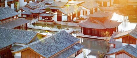 A traditional Chinese courtyard with multiple buildings, a central water feature, and a wooden bridge.