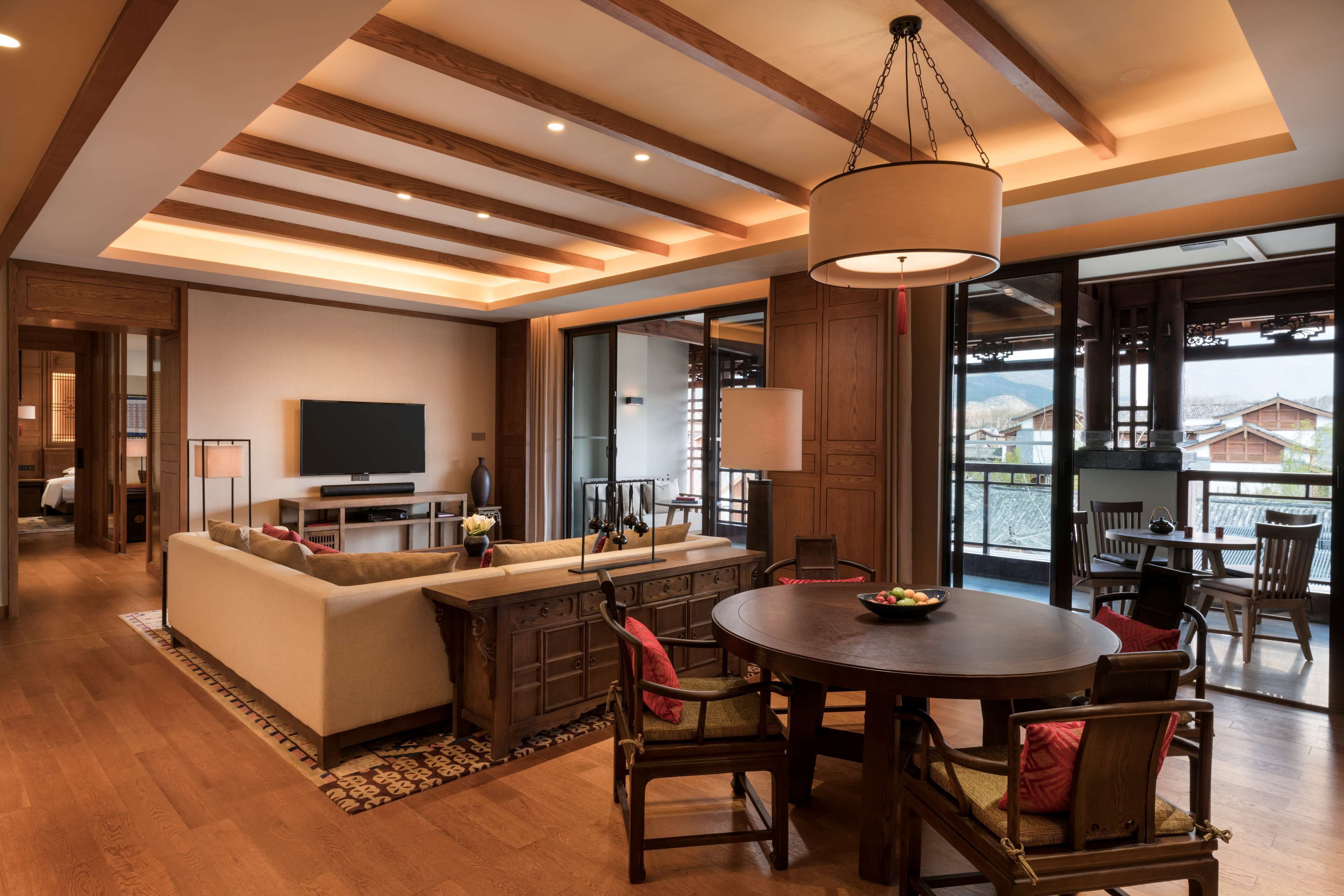 A spacious living area with a large sofa, dining table, and chairs, a television, and a view of the outside.